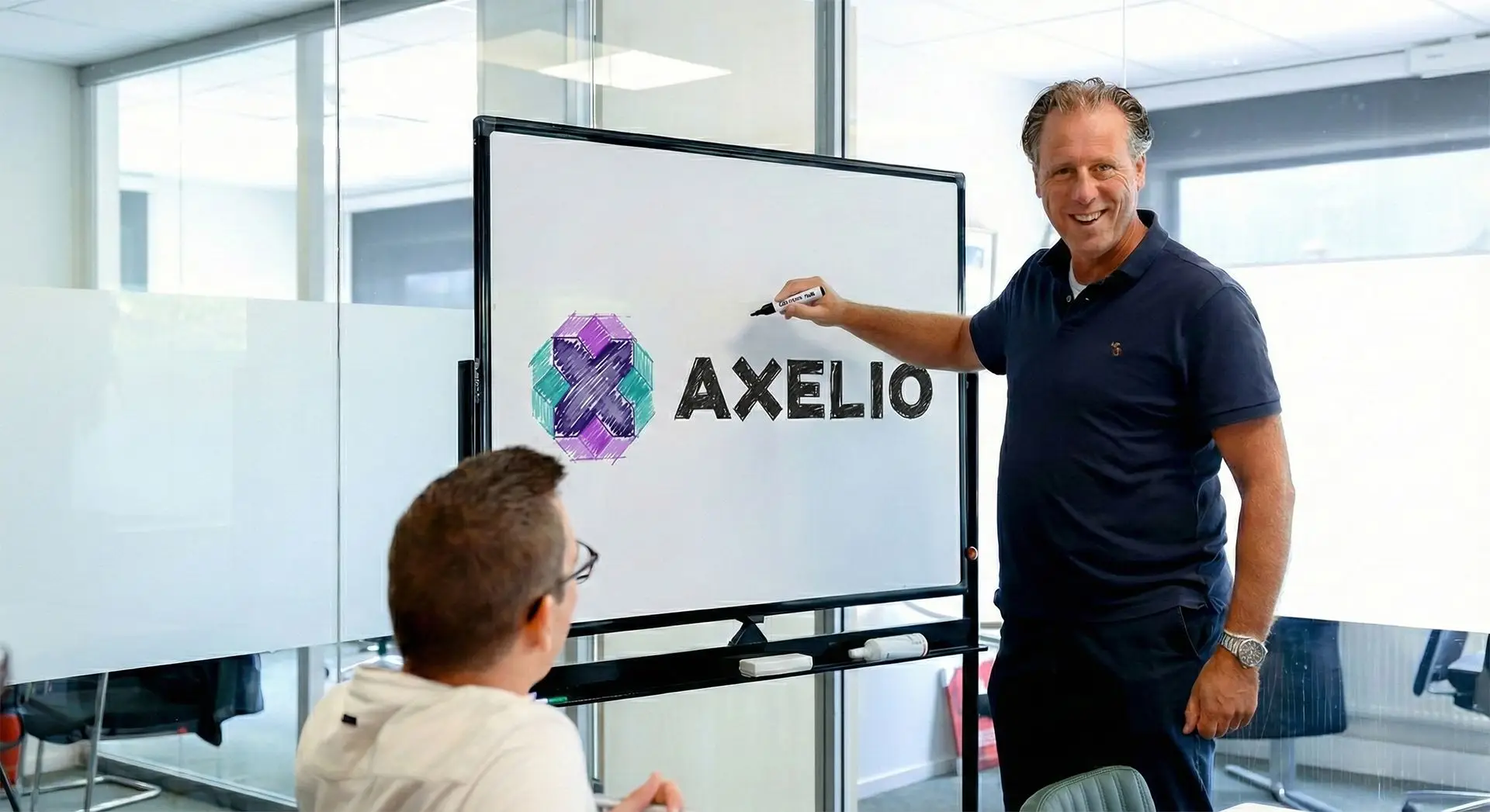 Een man in donkerblauwe polo die wijst naar een whiteboard