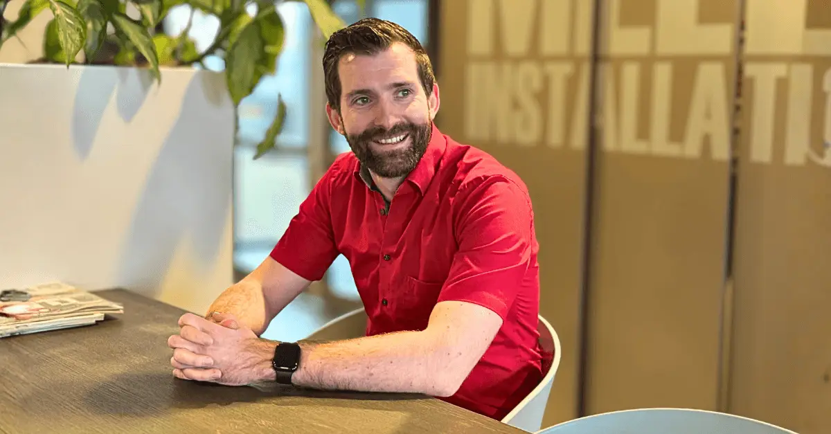 Een lachtende man met baard in rood overhemd met korte mouwen