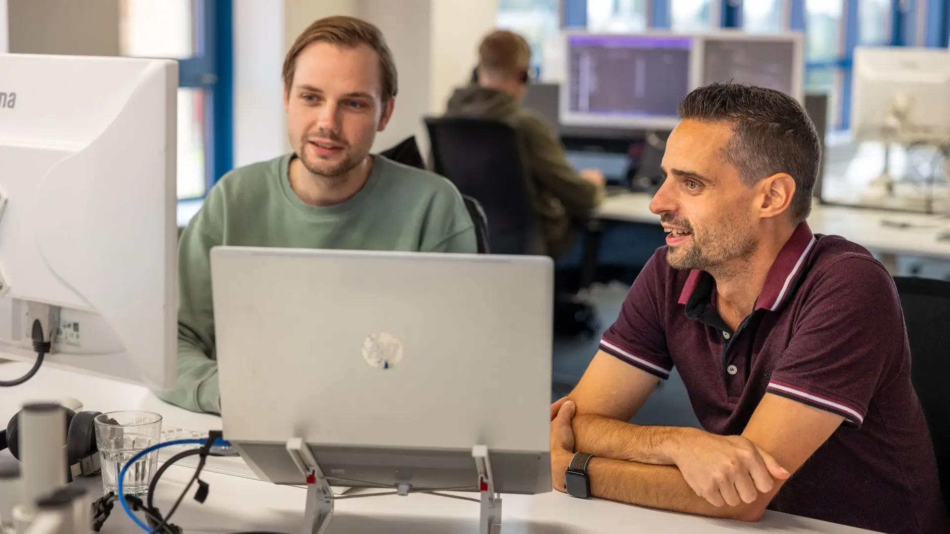 Twee pratende jonge mannen kijken naar computerschermen