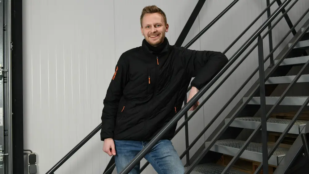 Een man staand op de trap en leunend op de trap leuning kijkt lachend in de camera