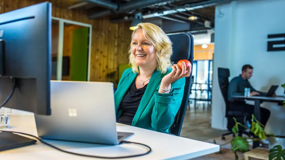 Een blonde vrouw met een appel in haar hand kijken en lachend naar een computerscherm