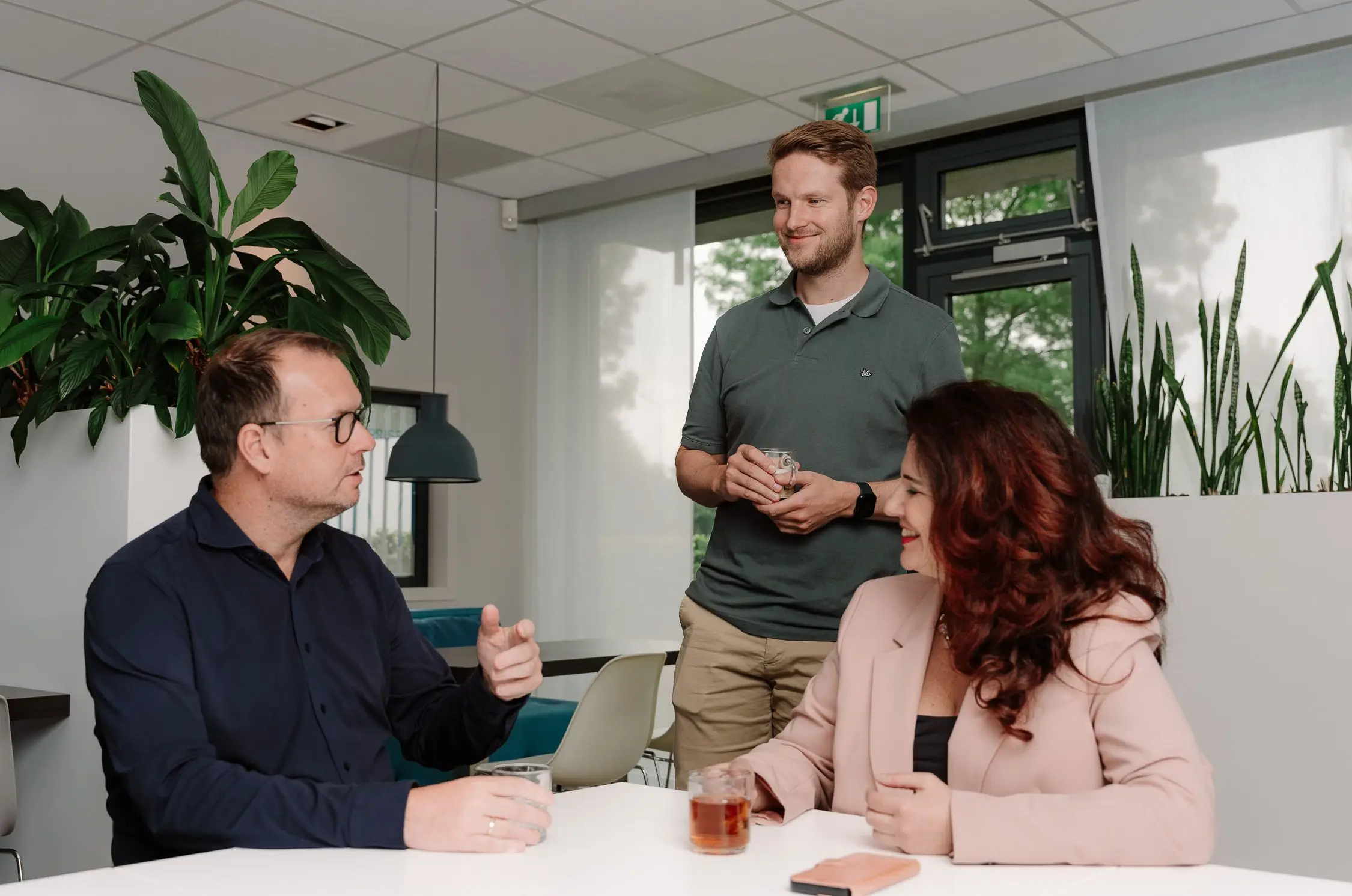 Maik Veenhuizen staat met koffie in de hand in gesprek met twee collega's aan tafel in de kantine van Axelio
