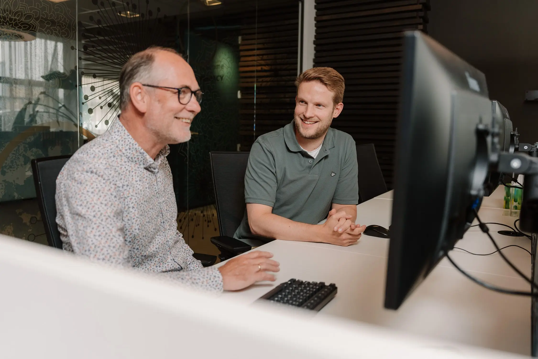 Maik Veenhuizen, Service Delivery Manager bij Axelio, lacht in gesprek met een collega achter de computer op kantoor